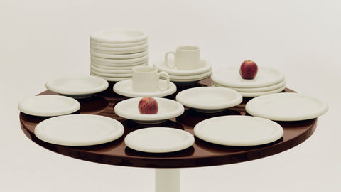 HAY Barro Plates and Cups in Off-White, glazed terracotta tableware laid out on a round dark brown table with two red apples