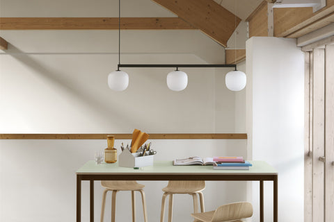 Muuto Rime Rail Lamp in Black with three glass shades above a high table with wooden bar stools