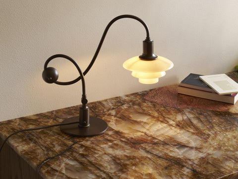 Louis Poulsen PH 1/1 Piano Table Lamp, Limited Edition, in aged brass with dusty terracotta glass shades, lit on a stone-topped cabinet beside books