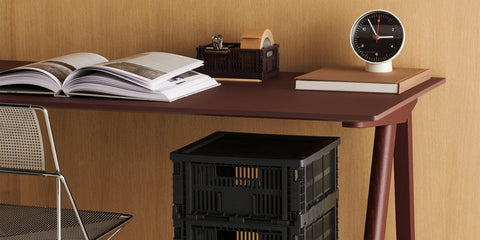 Colour Crate and table clock by HAY on a burgundy desk with an open book