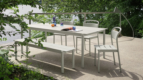 Linear Steel Outdoor Dining Table, Bench, and Side Chairs by Thomas Bentzen for Muuto in grey, set on a lakeside patio