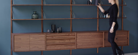 Royal System wall shelving by Poul Cadovius for DK3 in walnut with brass hangers above a row of walnut cabinets, against a blue wall