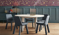 Blu Dot Good Times round dining table in white oak with four blue velvet chairs in a moody dining room with patterned wallpaper
