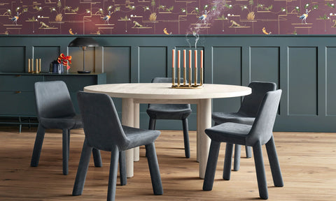 Blu Dot Good Times round dining table in white oak with four blue velvet chairs in a moody dining room with patterned wallpaper