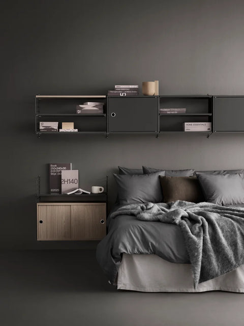 Bedroom with String® System modular shelving in grey and oak cabinets with flip doors, styled above and beside a bed with grey bedding