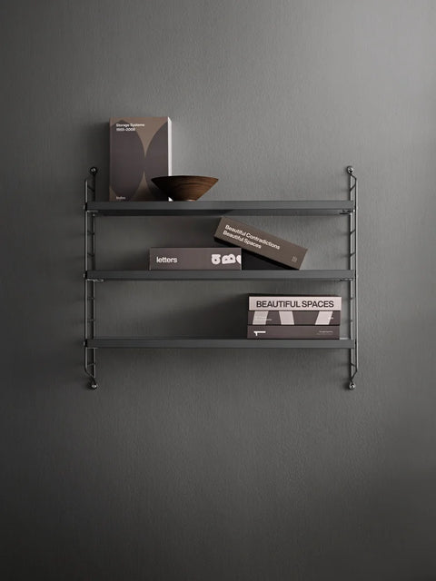 Dark grey String® Pocket shelf styled minimally with books and a wooden bowl against grey wall