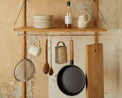 Frama Shelf Library Add-on Hanger Section in Natural Oak, oak shelf on a worn plaster wall with a pan, sieve, grater and mug hanging below