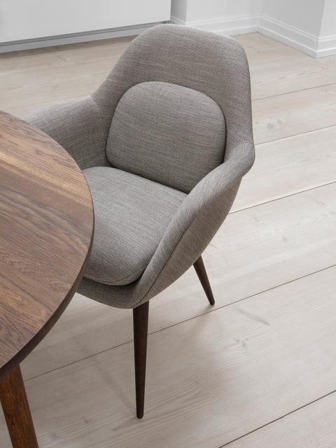 Swoon Dining Chair with wood base in grey upholstery beside a round walnut dining table by Fredericia.