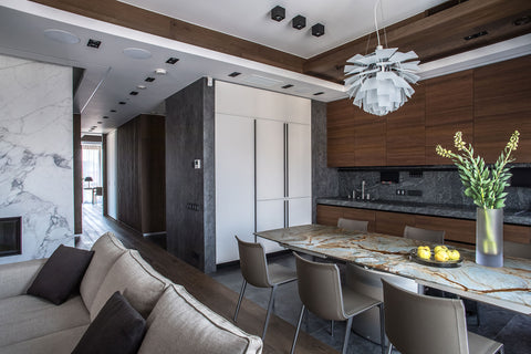 PH Artichoke pendant above a stone dining table in a sleek kitchen with walnut cabinets integrated appliances and grey stone backsplash