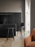 Fredericia Spine Barstool with Backrest in black leather beside matching backless stool in Scandinavian kitchen