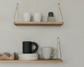 Frama Single Shelf, Natural Oak in Brass, two oak shelves on brass brackets holding cups, a black mug and stacked plates