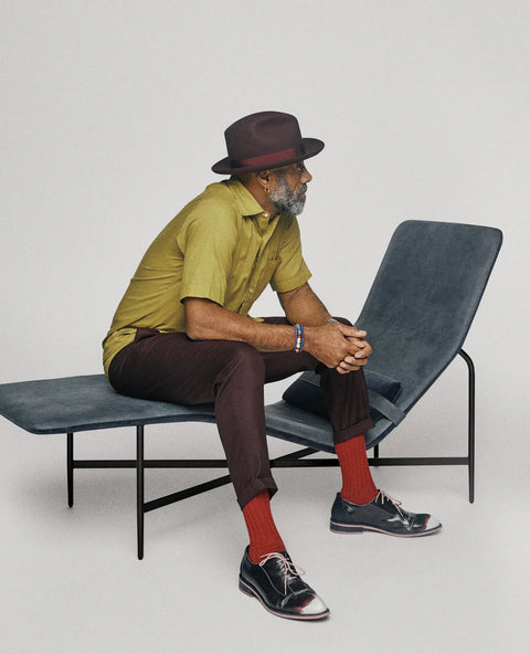 Blu Dot Deep Thoughts Chaise with a man in a fedora and olive shirt seated on the edge, showing the sculptural silhouette and powder-coated steel base