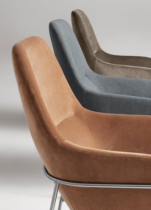 Blu Dot Acre Lounge Chair in camel velvet with brushed steel legs, styled in a warm wood-paneled reading nook with a black floor lamp and turned walnut side table