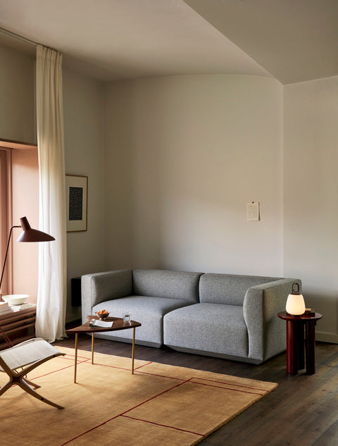 Living room with &Tradition Pinwheel HM7 End Table in walnut and brass beside a grey sofa and modern floor lamp