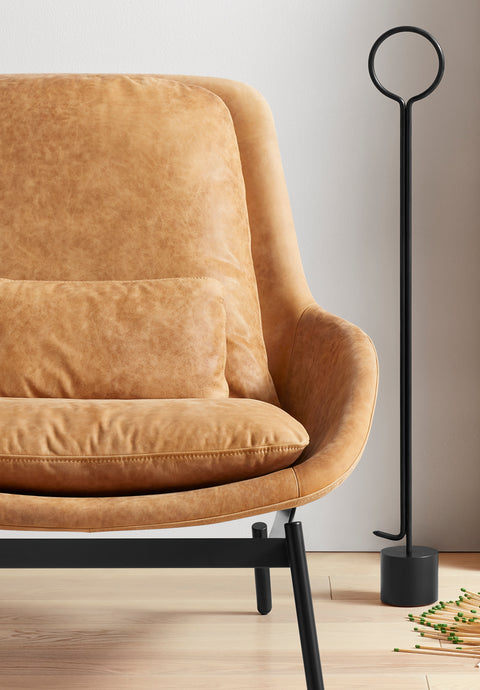 Blu Dot Field Lounge Chair in tan leather with black legs, shown in close detail beside a black sculptural floor lamp on light hardwood flooring