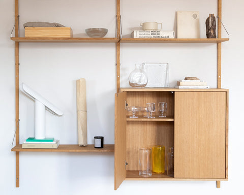 Frama Shelf Library Cabinet in Natural Oak, cabinet fitted into an oak shelf unit with one door open showing glasses, books and a lamp above