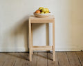 Frama Stool 01 in Natural Birch, pale birch stool holding a bowl of fruit against a plaster wall above a worn plank floor