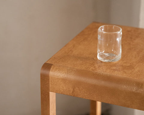 Frama Stool 01 in Warm Brown Birch, close view of the seat corner with its rounded edge and a glass tumbler standing on top