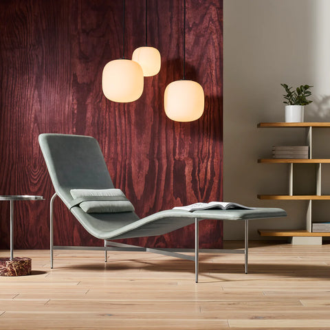 Blu Dot Deep Thoughts Chaise styled in a modern living room against a rich wood-grain wall with white globe pendant lights and an open book resting on the seat