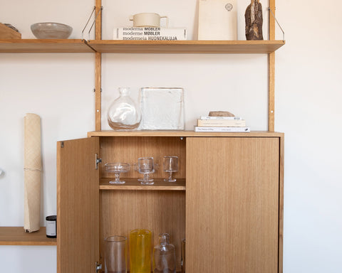 Frama Shelf Library Medium Cabinet Add-on Section in Natural Oak, cabinet with a door open showing glasses and bottles, objects on the shelf above