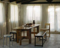 Frama Farmhouse Trestle Table in Natural Oak, long oak plank table on trestles in a room with sheer curtains, chairs, a bench and a metal stool