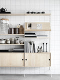 String Furniture cabinet with sliding doors in ash, Scandinavian modular storage styled with books and kitchenware