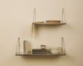 Frama Single Shelf, Stainless Steel, two steel shelves on a pale wall holding a woven bowl, books, a cup and a hanging cloth
