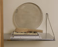 Frama Single Shelf, Stainless Steel, shelf holding a stack of books and a wooden paddle with a round metal tray leaning behind