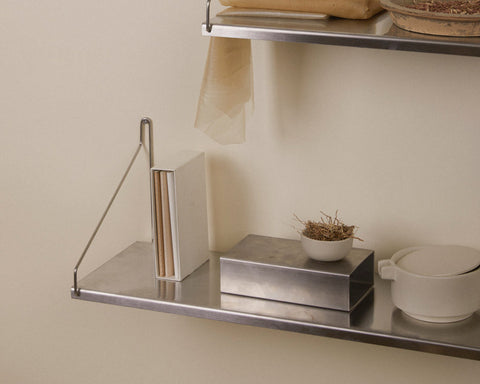 Frama Single Shelf, Stainless Steel, close view of a shelf with a metal box, a pot of dried grass and a bowl, plates above