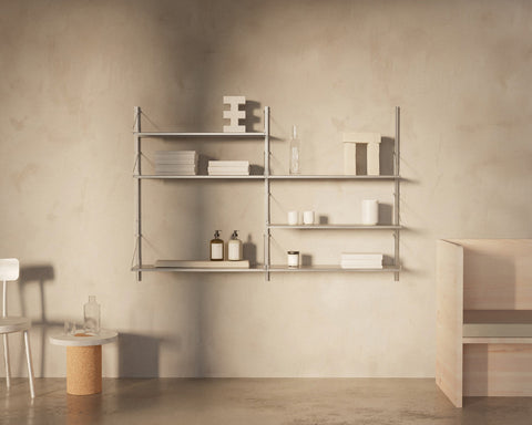 Frama Shelf Library Double Section in Stainless Steel, steel shelving on a plaster wall holding folded towels, bottles and cups, chair to one side