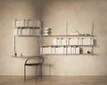 Frama Shelf Library Triple Section in Stainless Steel, wall of steel shelves filled with white books above a dark curved back chair