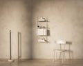 Frama Shelf Library Add-on Section in Stainless Steel, narrow steel shelving on a plaster wall holding books and boxes, with a wooden chair nearby