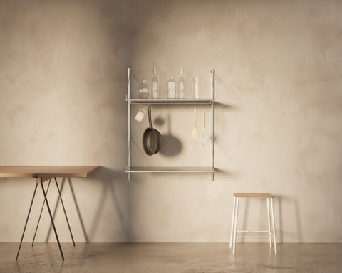 Frama Shelf Library Add-on Hanger Section in Stainless Steel, steel shelf holding bottles with a pan and utensils hanging, trestle table nearby