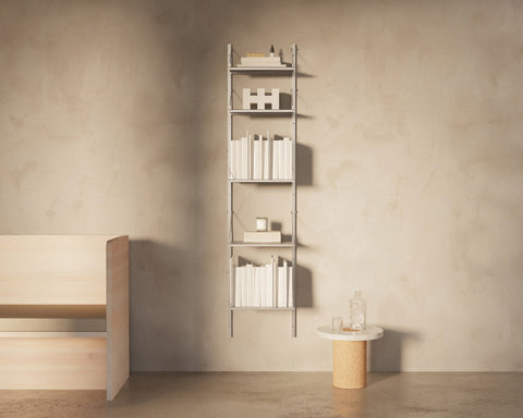 Frama Shelf Library Add-on Section in Stainless Steel, tall narrow steel shelving filled with books beside a wooden bench and a round side table