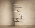 Frama Shelf Library Add-on Desk Section in Stainless Steel, tall steel unit with cups and books above a desk shelf holding an open book and a lamp