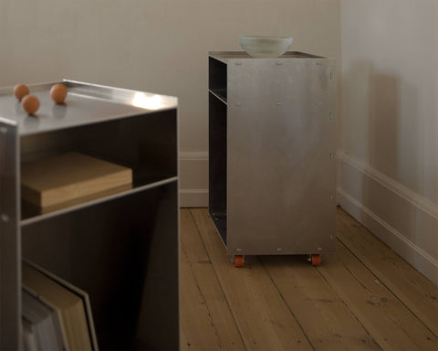 Frama Rivet Cart in Aluminum, two metal carts side by side against a plaster wall, one topped with a wooden board and handles