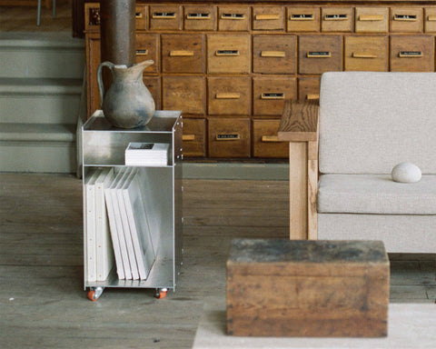 Frama Rivet Cart in Aluminum, metal cart holding upright magazines beside an apothecary chest, a jug resting on the rim