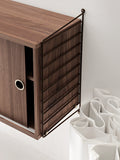 String Furniture cabinet with sliding doors in walnut finish, close-up view showing modular Scandinavian shelving detail