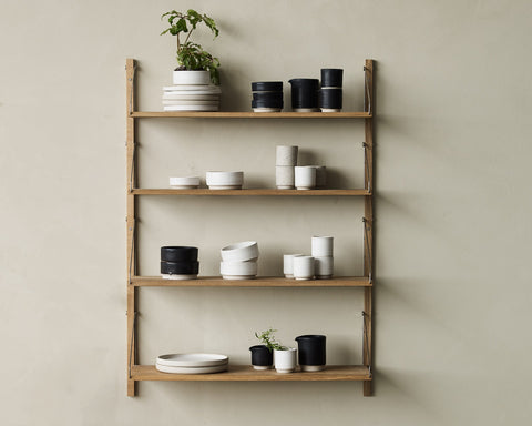 Frama Shelf Library Single Section in Natural Oak, oak shelves on a sage wall holding plates, black and white pots and a plant