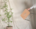 Frama Adam Stool, a hand lifting the leather seat top by its slot handle in front of a draped cloth and a potted plant