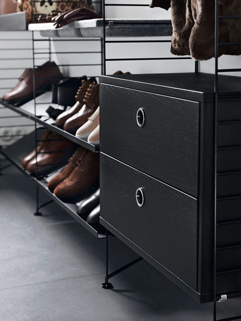 Black String® System chest of drawers with two drawers in a hallway storage unit, styled with shoes and outerwear
