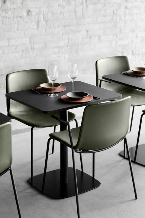 Close-up of green Pato Armchairs around black dining tables in a modern interior