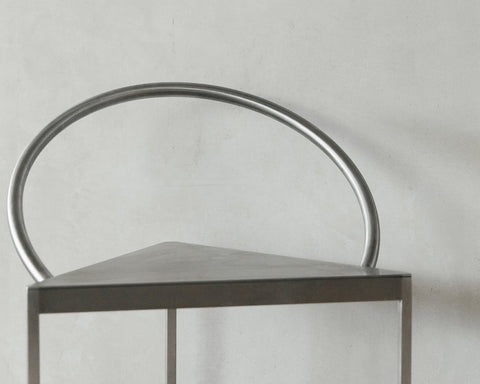 Frama Triangolo Chair in Stainless Steel, close up of the tubular hoop back rising from the triangular seat against a concrete wall