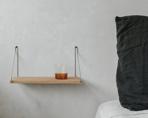 Frama Single Shelf, Natural Oak in Stainless Steel, oak shelf on steel brackets holding a tumbler of amber drink beside a dark cushion