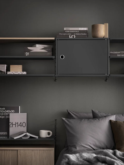 Dark grey Cabinet with Swing Door integrated into String® System shelving above bed