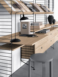 String Furniture oak shelving system with integrated desk, drawers, and black wire panels