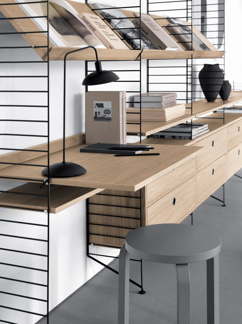 String Furniture oak shelving system with integrated desk, drawers, and black wire panels