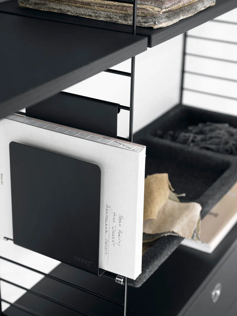 Black String® Magazine Holder attached to modular shelving with books and fabric samples