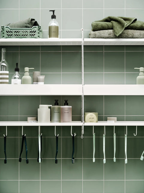 String® System low white metal shelves in bathroom, styled with toiletries, green towels, and hanging toothbrushes