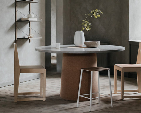 Frama Chair 01 in Natural Birch, pale birch chairs at a round stone topped table with a vase and metal stools in a grey room